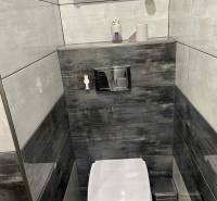 Toilet in a 3-room apartment with dark tiles and a wall-mounted towel holder.