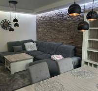 Living room with a corner sofa, hanging lamps, and decorative stone cladding in a 3-room apartment.