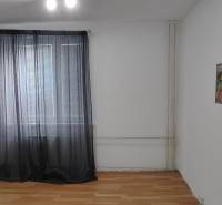 A room with a wooden decor floor and a painting in a three-room apartment, curtains on the windows.