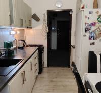 A kitchen with a wood-patterned floor, a kitchen unit, and a refrigerator in a three-room apartment.