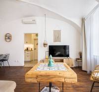 Living area of a studio apartment with a wooden decor floor, a table, and a television.