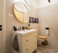 Bathroom in a studio apartment with a round mirror, patterned tiles, light-colored tiles.