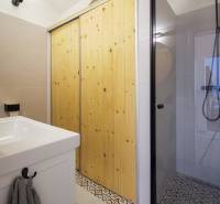 Bathroom with a glass shower enclosure, wooden doors, and light tiles in a studio apartment.