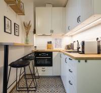 A kitchenette of a one-room apartment with white cabinets, patterned floor, and wooden shelves.