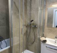 A shower corner with marble tiles in a 4-room apartment, next to a sink with a white cabinet.