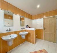 A bathroom in a family house with orange and white tiles, a double sink, and mirrors.
