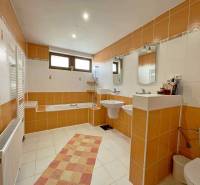 A bathroom in a family house with orange and white tiles, a bathtub, and a sink.