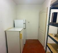 A narrow room in a catering area with refrigerators and a metal shelf.
