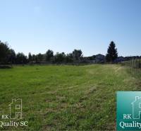 A grassy residential plot on Vrbová Street in Jelka, surrounded by trees and fencing.