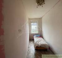A narrow room in a family house with a bed, a window, and ceramic flooring.