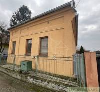 An orange family house in Neded surrounded by a fence, next to trees and other houses.