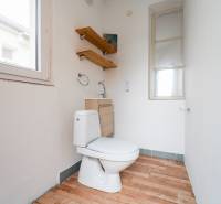 A toilet in a family house with a wooden decor floor and white walls.