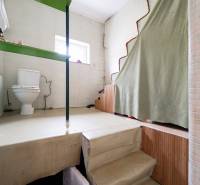 A bathroom in a family house with a toilet and stairs, covered by a green curtain.