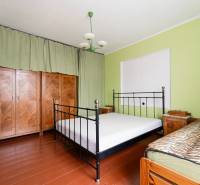 Bedroom in a family house with a metal bed, wooden wardrobe, and green walls.