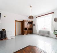 Living room in a family house with furniture, wooden decor, a stove, and white walls.