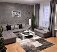 Living room with a large gray sofa, decorative wallpaper, and wood-patterned flooring.
