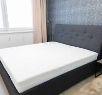 A bedroom with a gray bed, patterned wallpaper, and a nightstand.