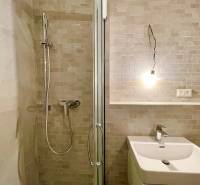 Bathroom in a 2-room apartment with a sink, shower, and light on beige tiles.
