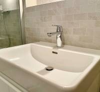 Bathroom in a 2-room apartment with a sink and a shower stall with glossy tiles.