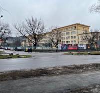 A city street in Košice with buildings, trees, and a road in rainy weather.