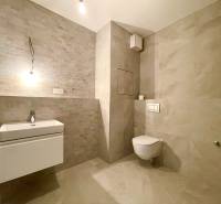 Bathroom with a wall-mounted toilet and sink in a two-room apartment with neutral tiles.