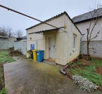 A family house on Mechenická Street in Podhorany with a concrete walkway, containers, and grass.