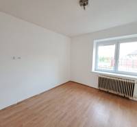 A room in a family house with white walls, a wood-patterned floor, and a large window.