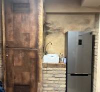 Rustic wall, next to a refrigerator and sink in commercial premises with wood-patterned flooring.
