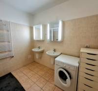 A bathroom in a 3-room apartment with mirrors, a washing machine, sinks, and light-colored tiles.