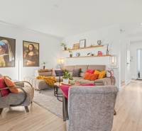 Living room of a family house with comfortable seating, decorative paintings, and a wooden-patterned floor.