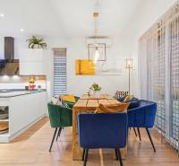 The dining room of a family house with a wooden table, colorful chairs, and a kitchen in the background.