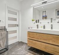 A bathroom in a family house with a dark stone floor, wooden decor of the cabinet under the sink.