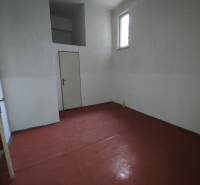 An office with a simple interior and a red floor, a small window, and white walls.