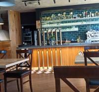 A café with a wooden decor floor, a bar counter, and brick elements in the gastro area.