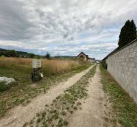 A dirt road surrounded by grassy residential plots on Poľnohospodárska Street in Trenčín.
