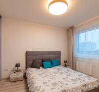 Bright bedroom with a bed, table, lamp, and wardrobe; floor with wood decor.