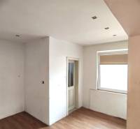 Interior of a family house with white walls, wood-patterned flooring, and a window.