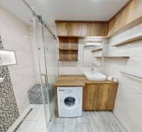 A bathroom in a 3-room apartment with a washing machine, shower cabin, and wooden decor furniture.