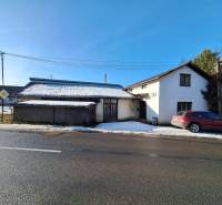 A building by the road with a snow-covered roof and a parked car in Medzany.