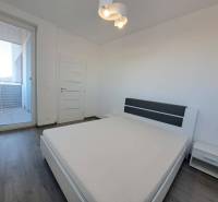 A bright bedroom in a two-room apartment with white furniture and a wooden decor floor.