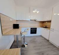 A kitchen in a 2-room apartment with white cabinets and a wooden decor floor.