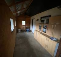 The interior of the cottage with simple furniture, a shelving cabinet, and basic kitchen equipment.