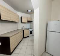 Kitchen area of a studio apartment with storage space and appliances, tiled floor, light shades.