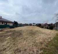 Building plot for housing in Hlohovec, grassy area between houses under a cloudy sky.