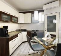 A kitchen in a 3-room apartment with modern furniture, a glass table, and a floor with a wood decor.