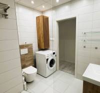 A bathroom in a 3-room apartment with a washing machine, light tiles, and a decorative wooden element.