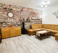 Living room in a three-room apartment with a brick wall, beige sofa, and wooden decor flooring.