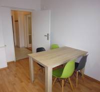 Dining area in a studio apartment with wood-patterned flooring and four chairs.