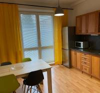 A kitchen in a studio apartment with yellow curtains and a wood-patterned floor.