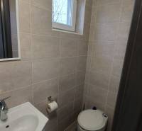 A bathroom in a cottage with a sink, toilet, and window, tiled with light tiles.
